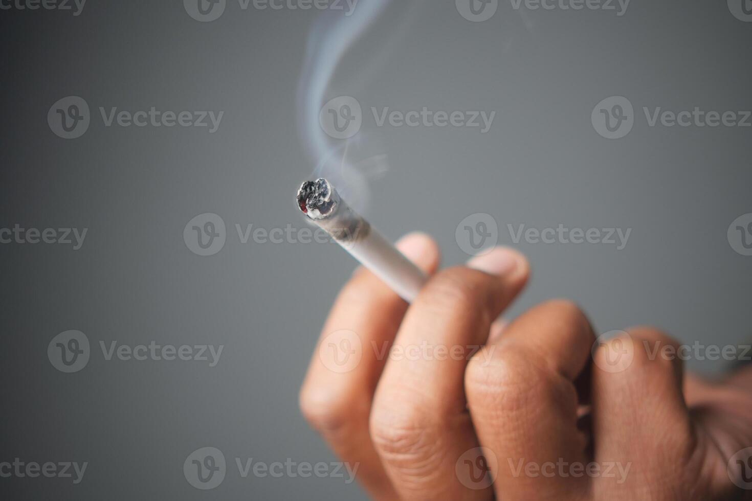 Close-up of a hand holding a burning cigarette in low light photo