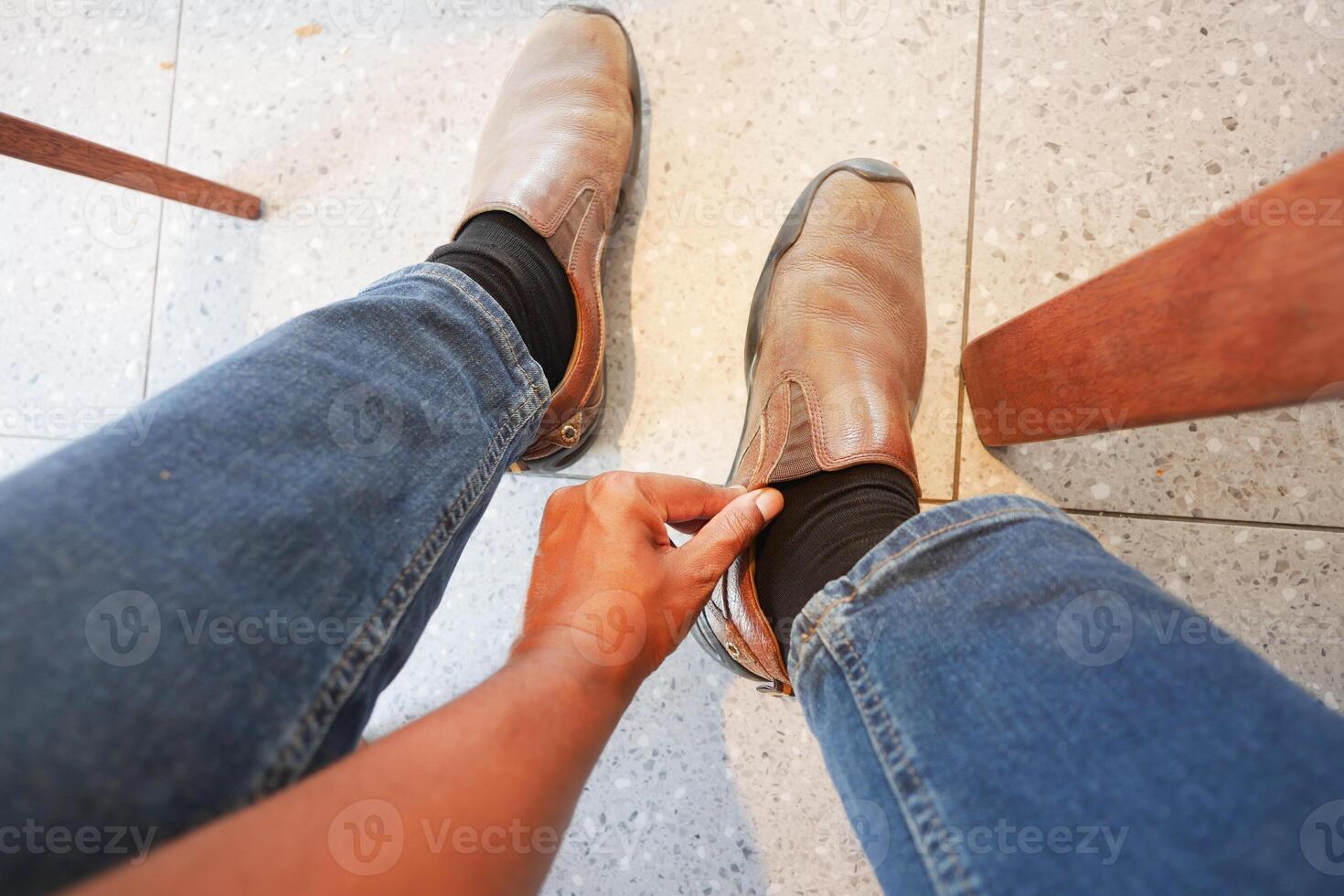 Person adjusting brown shoes while sitting on a chair indoors photo