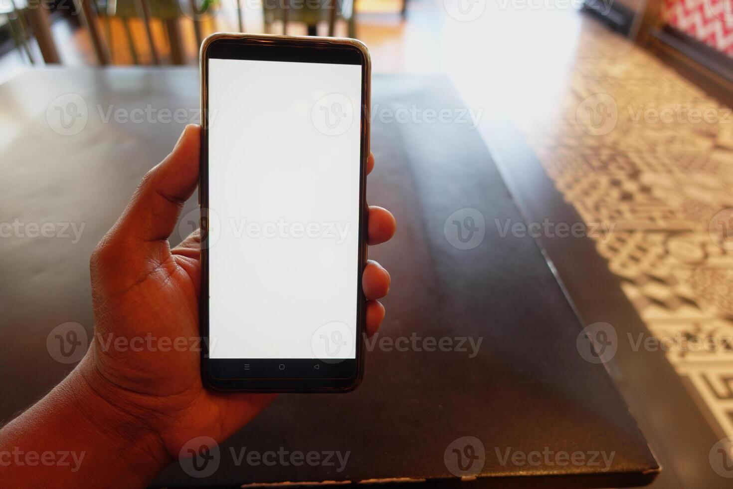 Hand holding a smartphone in a cafe setting during daylight hours photo