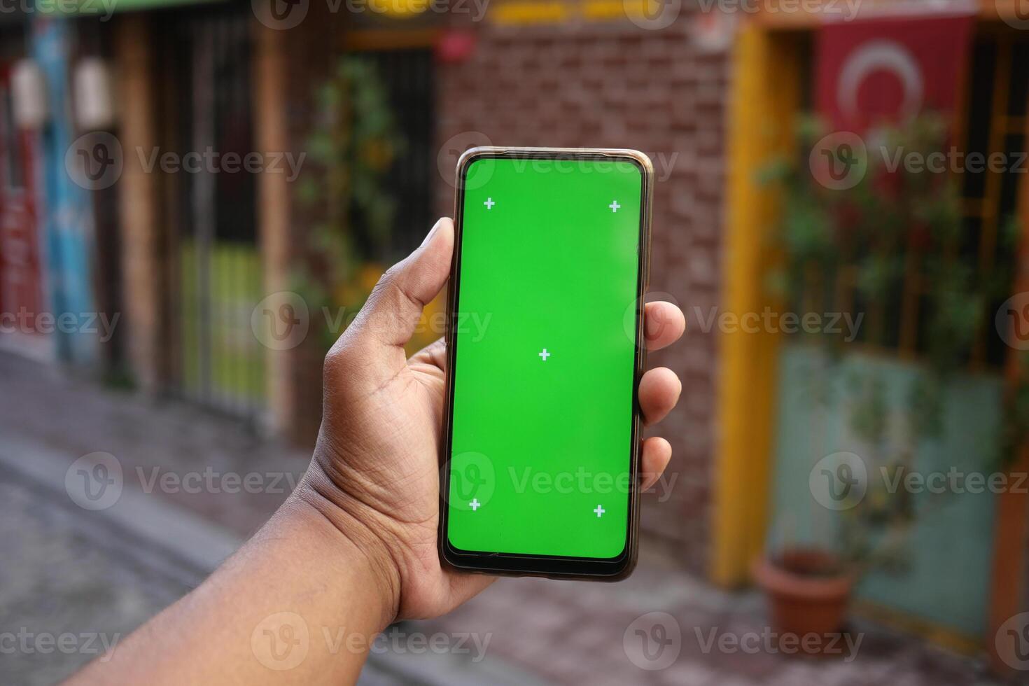 Hand holding a smartphone with a blank green screen outdoors photo