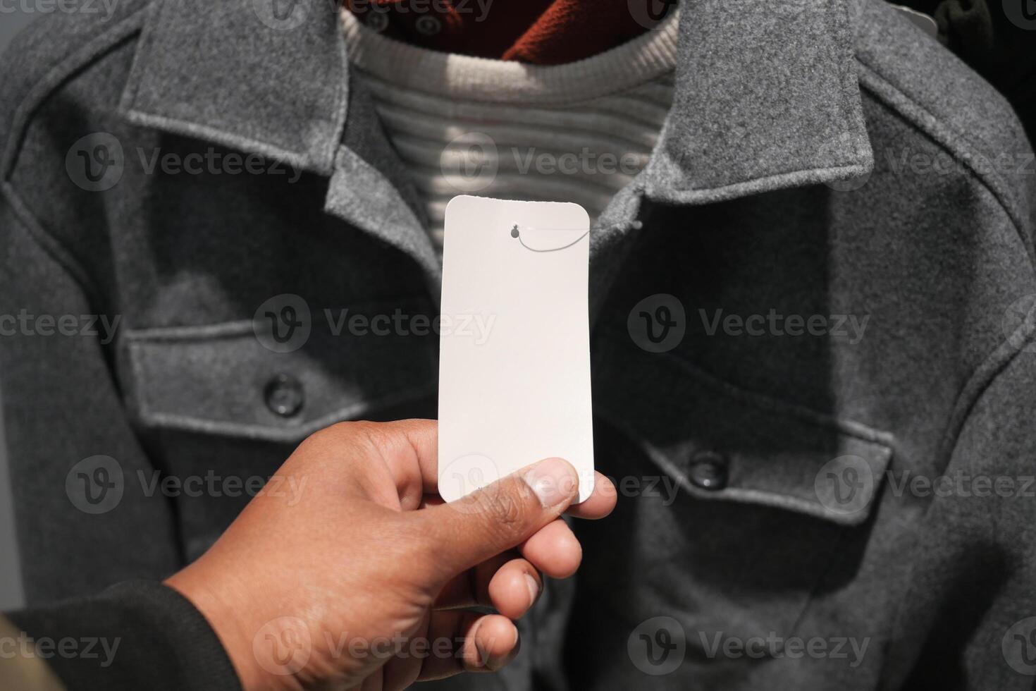 Hand holding a price tag near a gray jacket in a store display photo