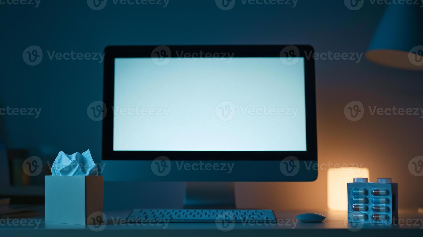 A dimly lit workspace featuring a blank computer screen, a tissue box, and a lamp, creating a calm and focused atmosphere. photo