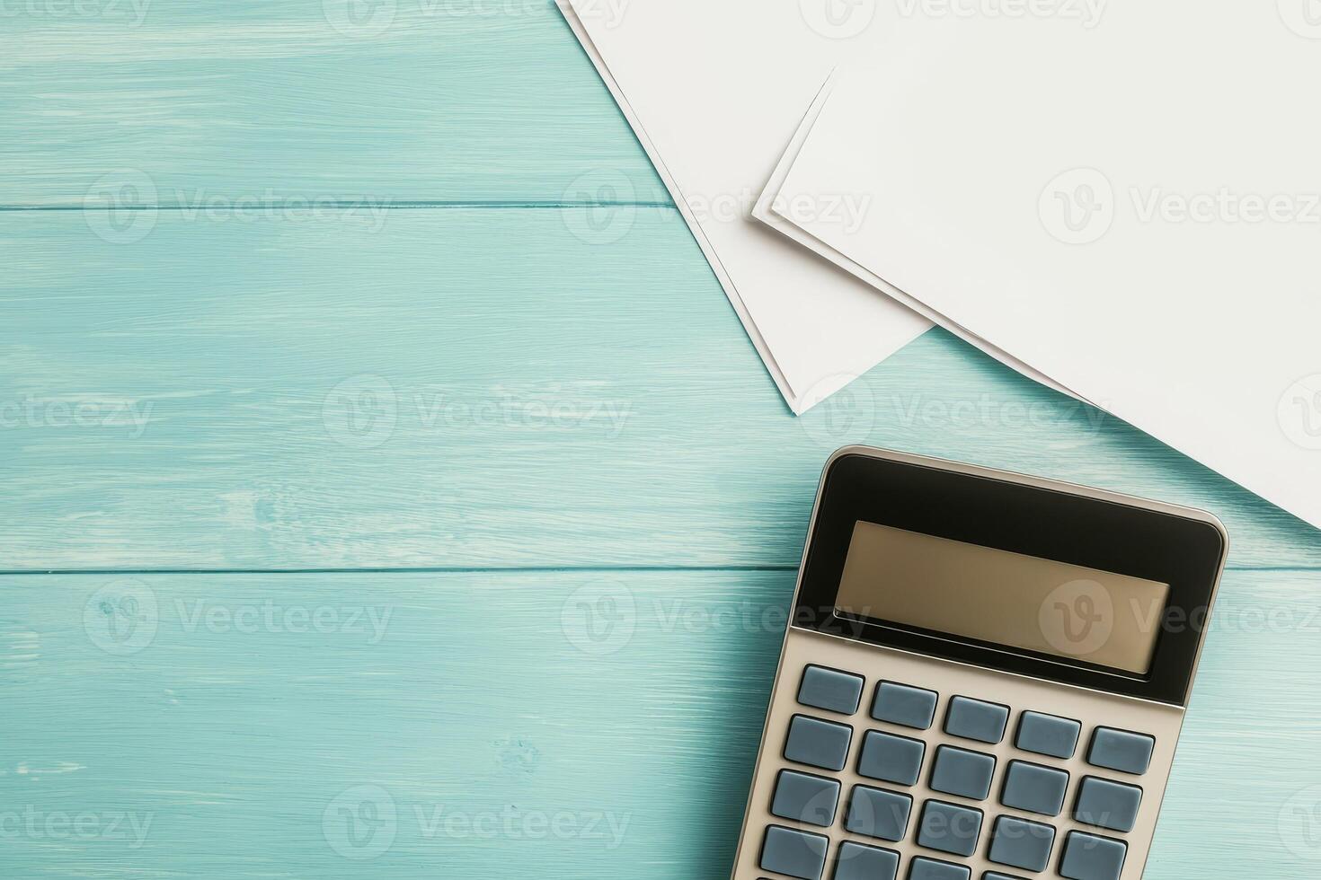 A top-down view of a calculator next to blank papers on a light blue wooden surface, ideal for math or financial tasks. photo