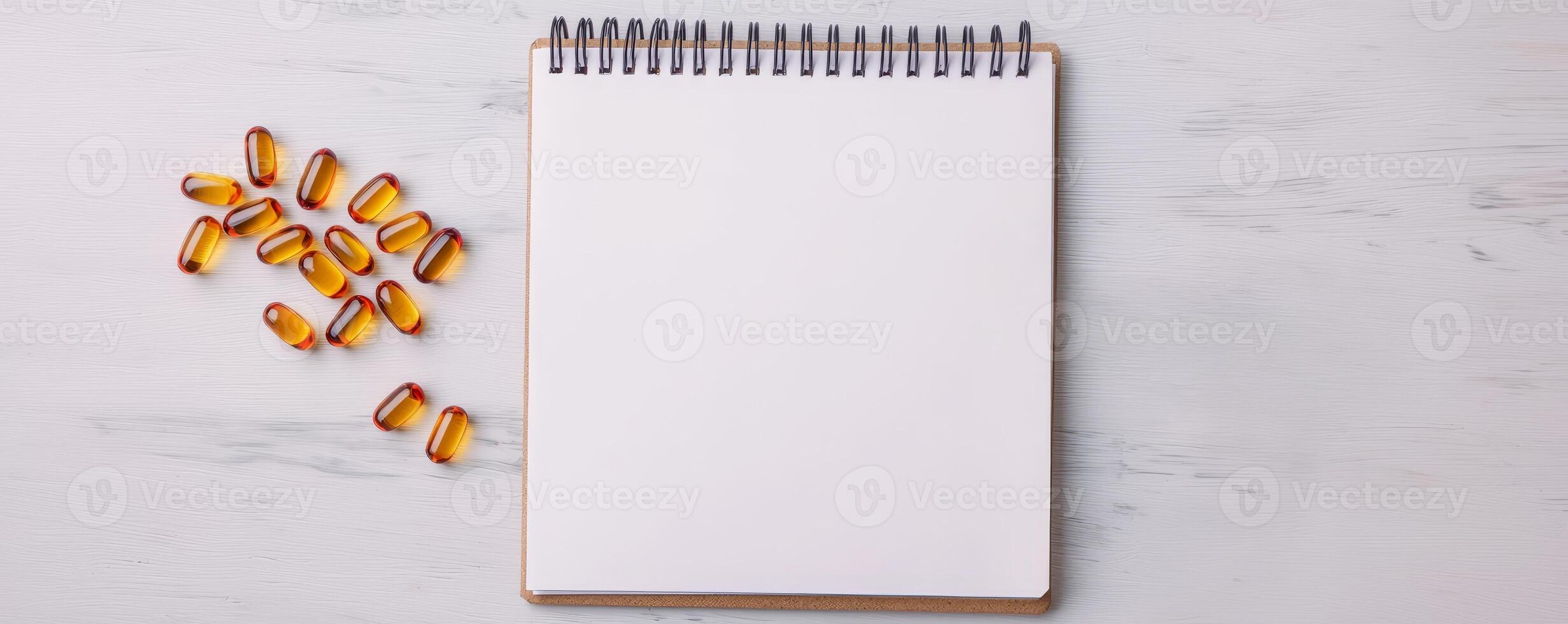 A blank notepad with a spiral binding sits on a light surface, accompanied by scattered golden capsules. photo