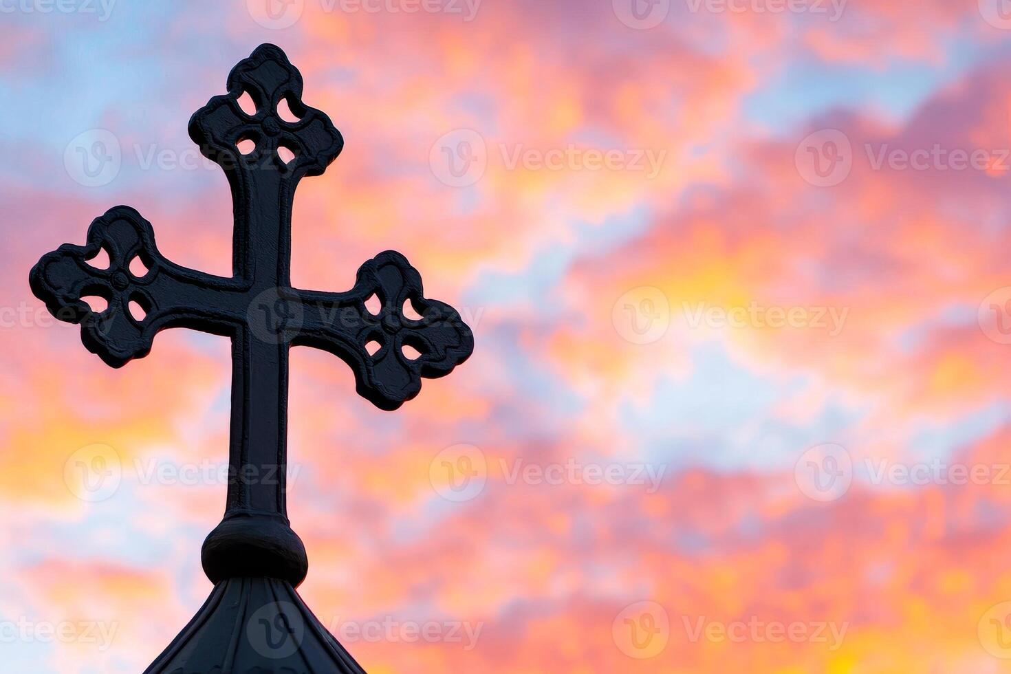 A silhouette of a decorative cross against a vibrant sunset sky, symbolizing spirituality and faith. photo