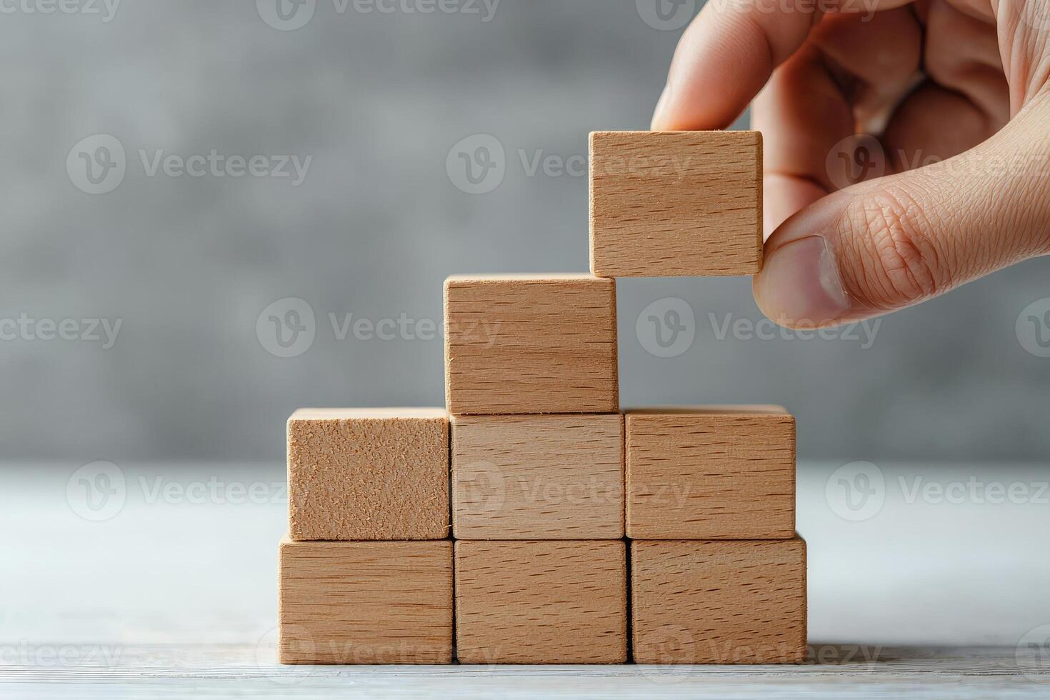 Motivation for entrepreneurship growth mindset concept. A hand stacking wooden blocks to create a pyramid shape on a textured surface. photo