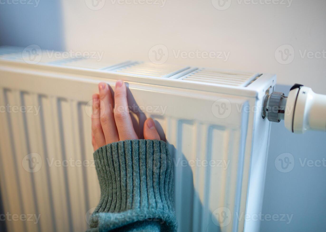 Woman warms up hands over heater. Concept of the need for good central heating. photo