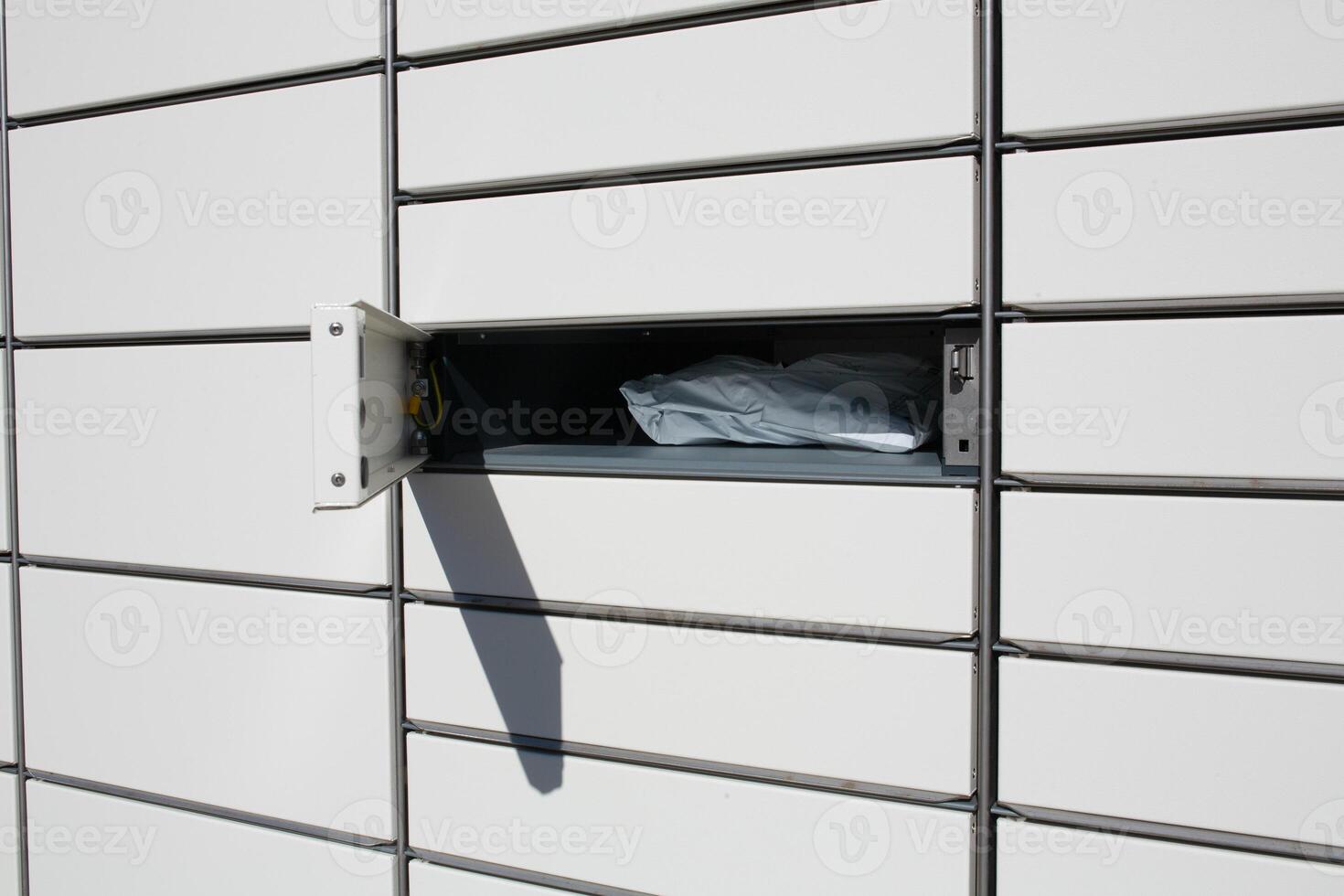 An open parcel locker cell with a delivered package. Sunlight, metal construction, modern parcel locker for order pickup. Concept of online shopping photo