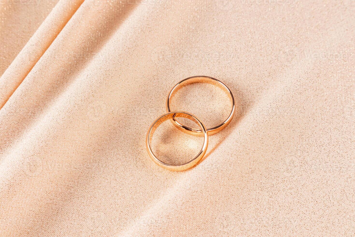 Two classic gold wedding rings lie on a chic gold-colored fabric with glitter. Soft folds of fabric flow from bottom to top. Wedding design. layout. photo