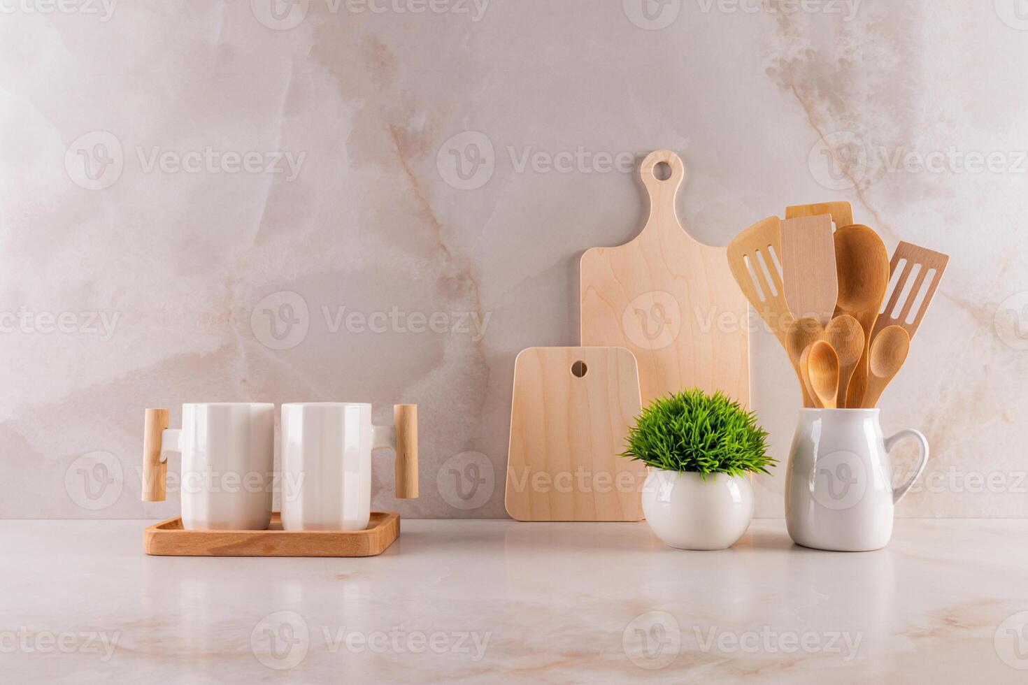 Two stylish white ceramic mugs, a cutting board set, a pitcher with wooden tools, and a potted flower on a marble countertop. kitchen background. photo
