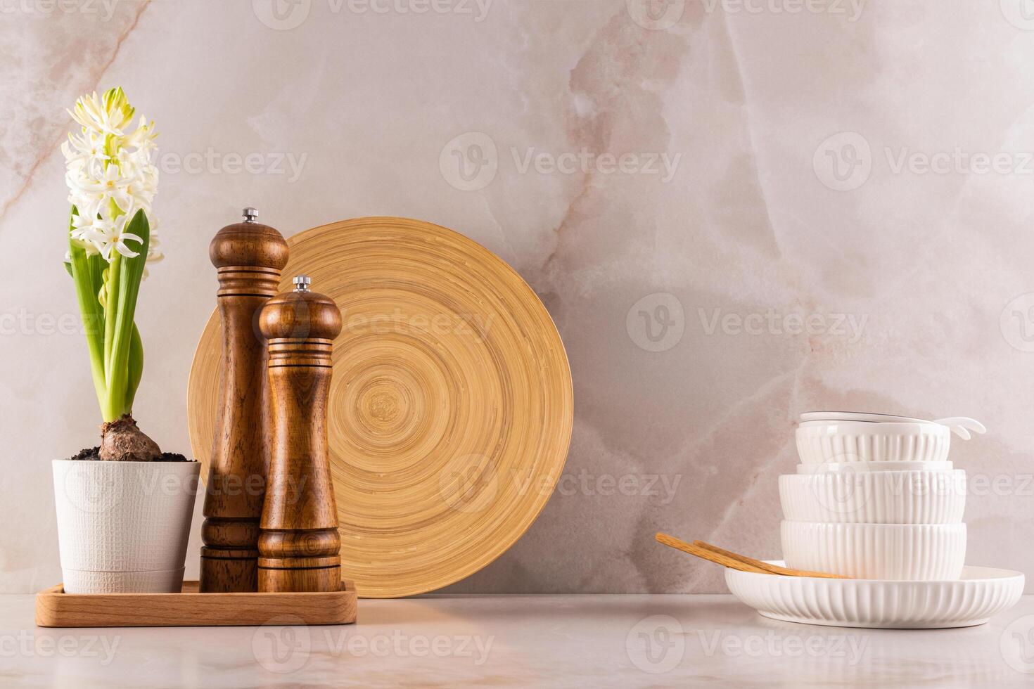 kitchen background in a minimalist style. two wooden spice grinders and white ceramic tableware on a marble beige countertop. Spring flowers in a pot. photo