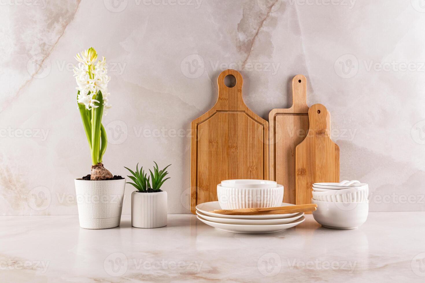 Beautiful spring still life on a marble kitchen countertop. A set of wooden cutting boards, white bowls and a flower in a pot. Front view. photo