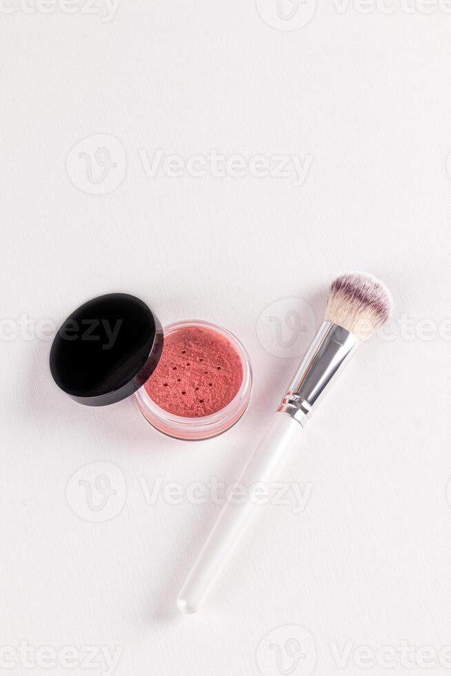 An open cosmetic jar with pink dry blush and a chic fluffy makeup brush on a white background. top vertical view. layout for advertising the product photo