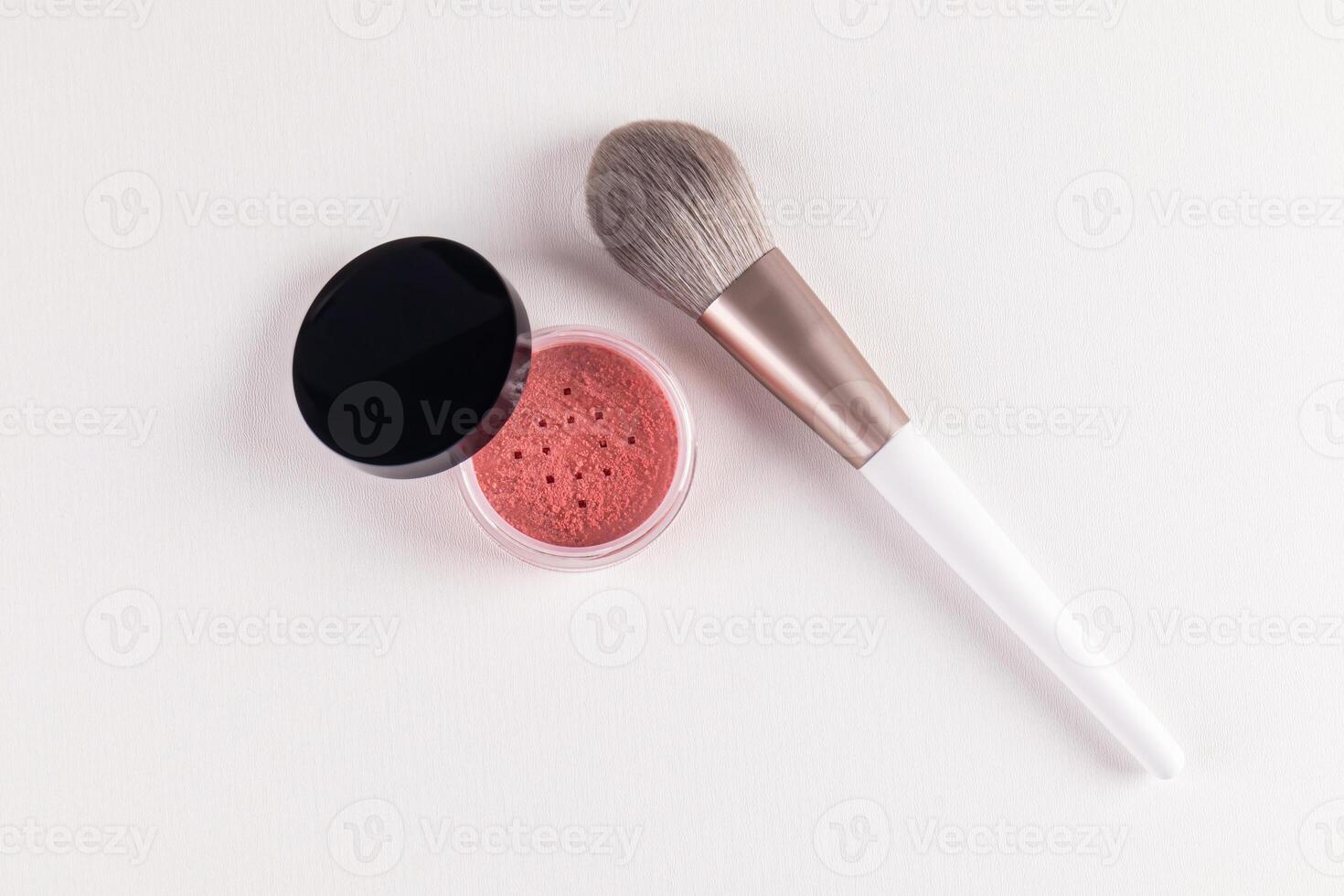 An open cosmetic jar with pink dry blush and a chic fluffy makeup brush on a white embossed background. top view. layout for advertising the product photo