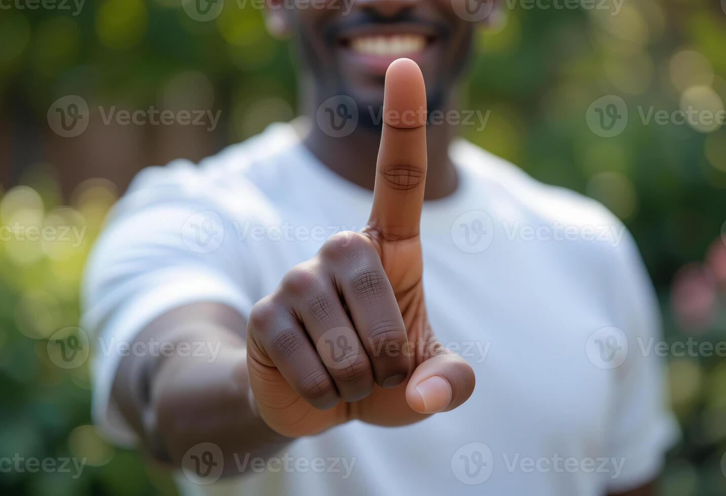 Smiling Affrican American Man in White T-Shirt Pointing at Camera in Green Outdoor Garden photo