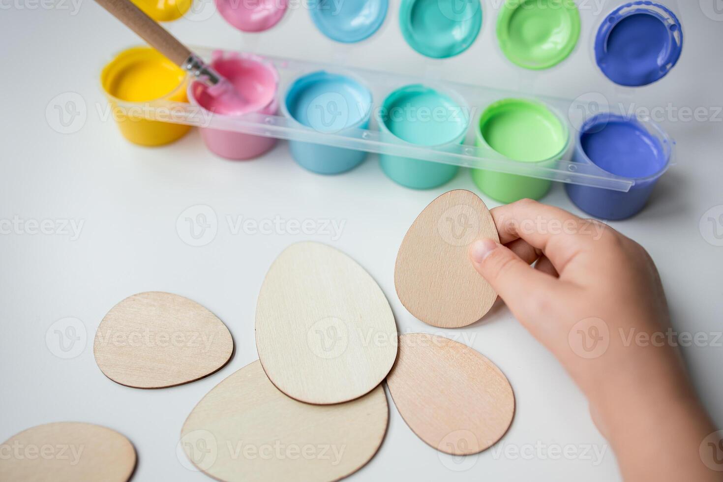 Child hand holding Easter wooden egg shapes with colorful paints for Easter crafting photo