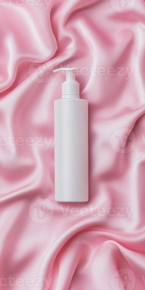 Minimalist flat lay of glossy white bottle on soft pink satin background for skincare design photo