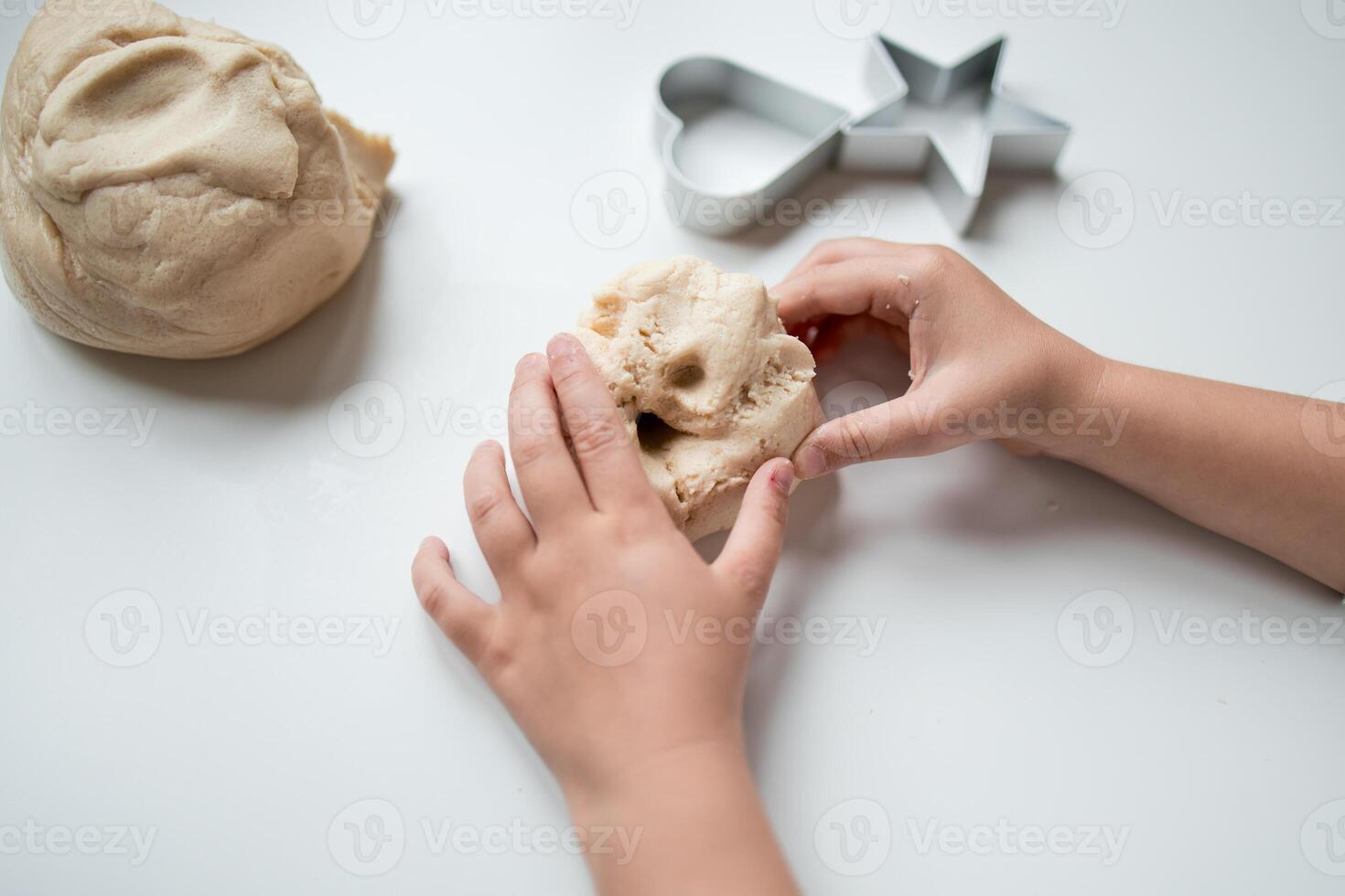 Child hands kneading dough with heart and star cookie cutters on white surface photo