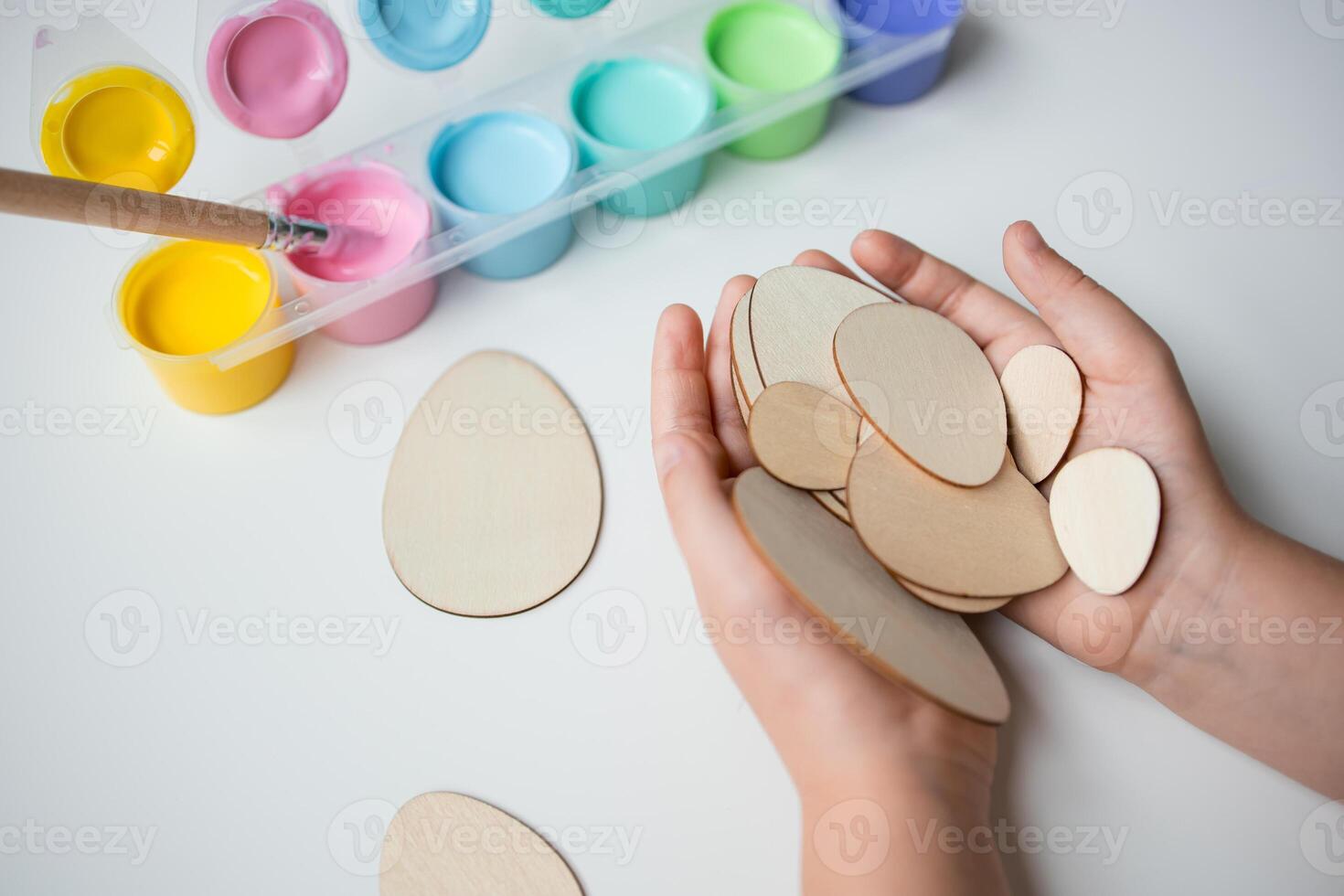 Child holding wooden Easter eggs with colorful paint set for creative crafting photo