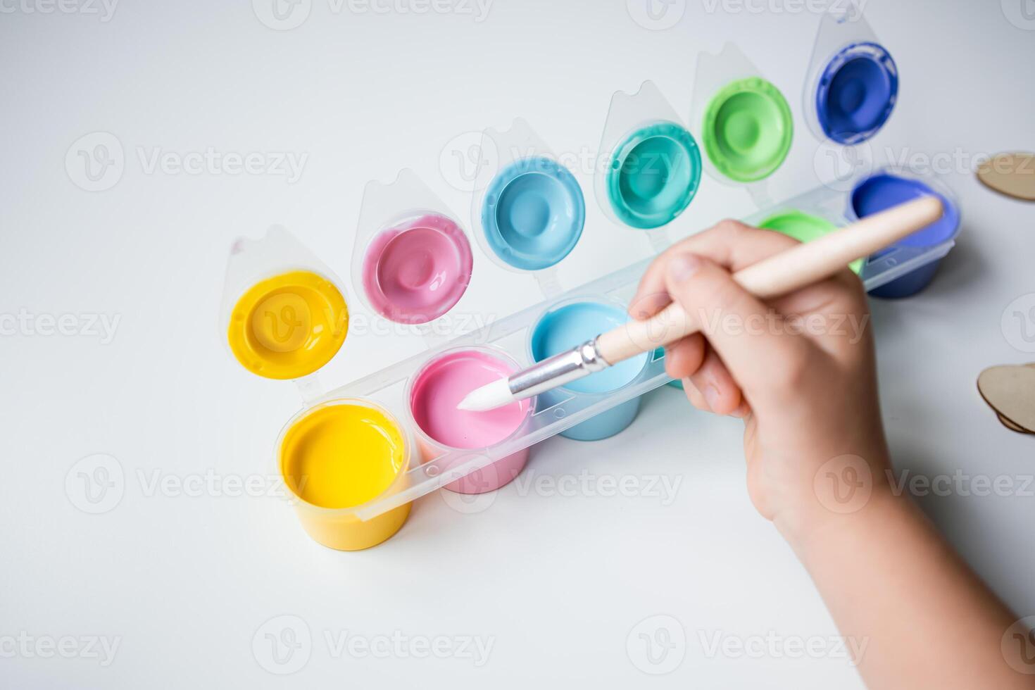 Childs hand holding brush over pink paint with bright color palette photo