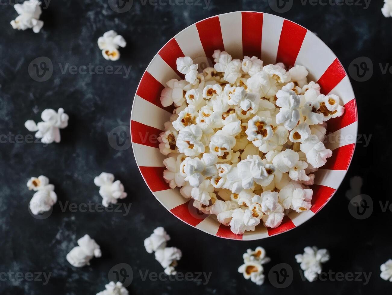 Salted popcorn in striped bowl overhead spill on dark surface for snack themed designs photo