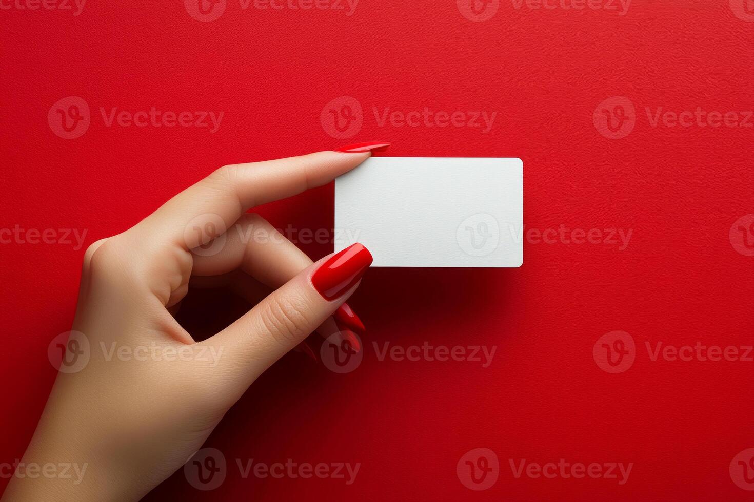 Female hand with red nail polish manicure is holding a blank white business card on a red background photo