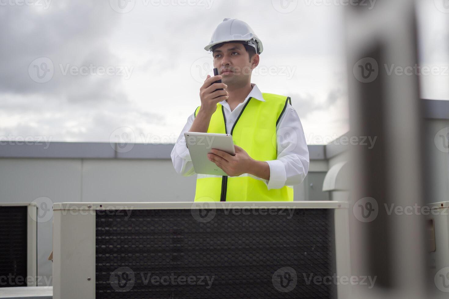 Asian maintenance engineer works on the roof of factory. contractor inspect compressor system and plans installation of air condition systems in construction. technology, online, mobile application photo