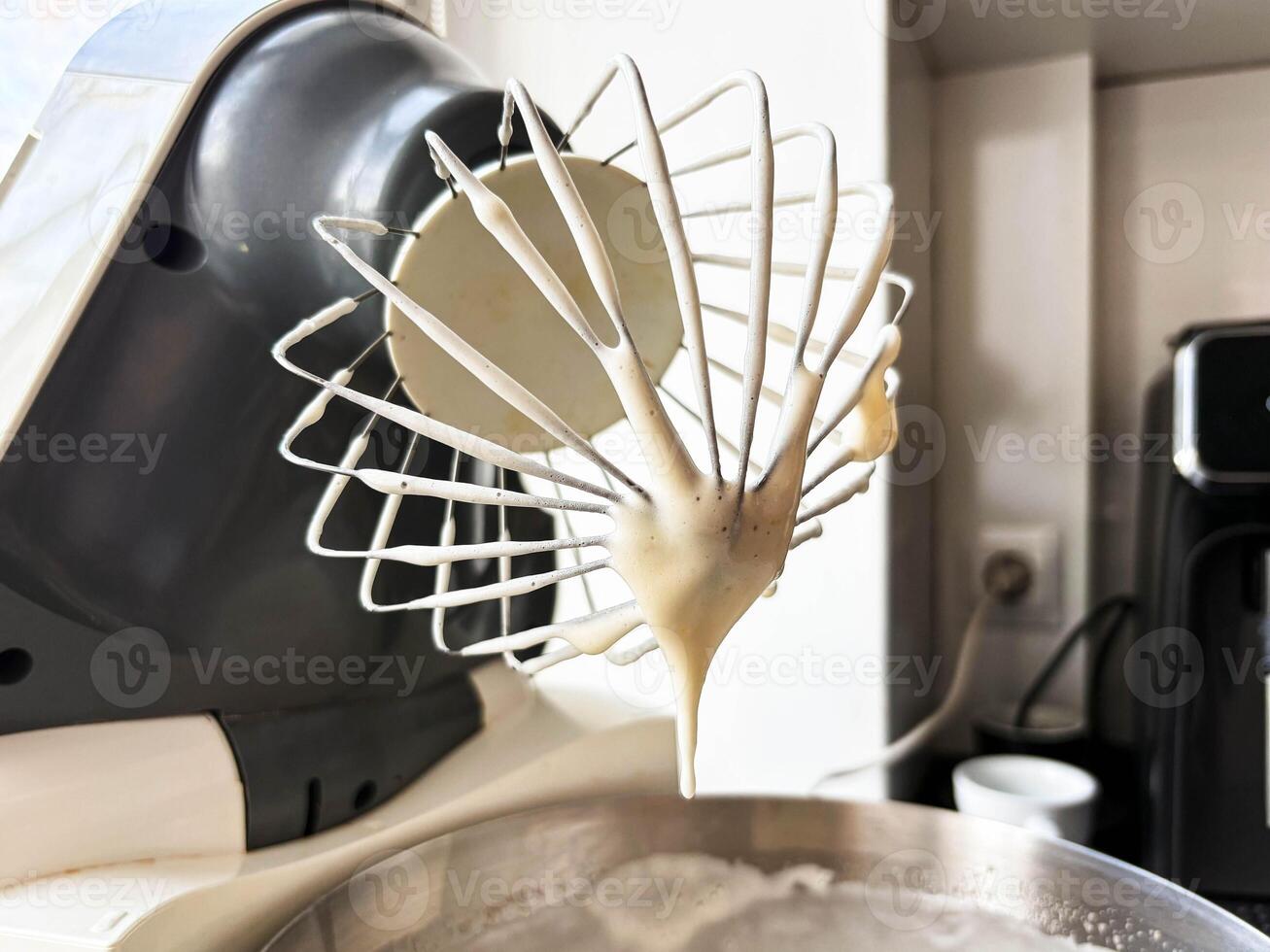 The whipped dough flows from the whisk of a stationary food processor, which sits on the kitchen counter. Kitchen assistant. photo