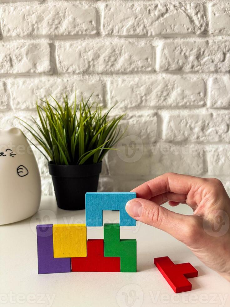 Female hand assembling wooden cube puzzle on white background with potted plant in background. photo