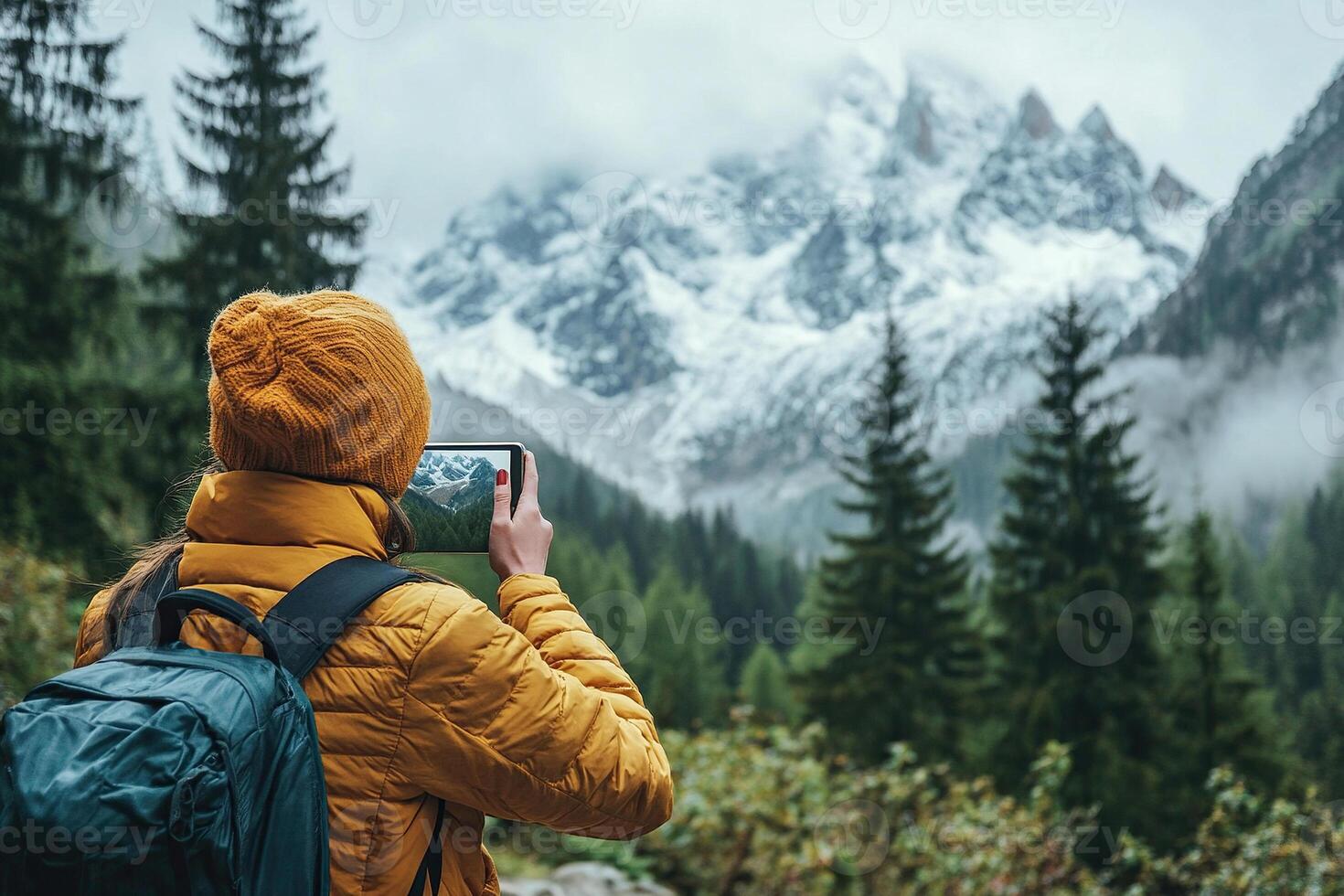 A female tourist in a yellow jacket and with a backpack on her back takes a photo on a smartphone in the mountains. A female tourist during her vacation.