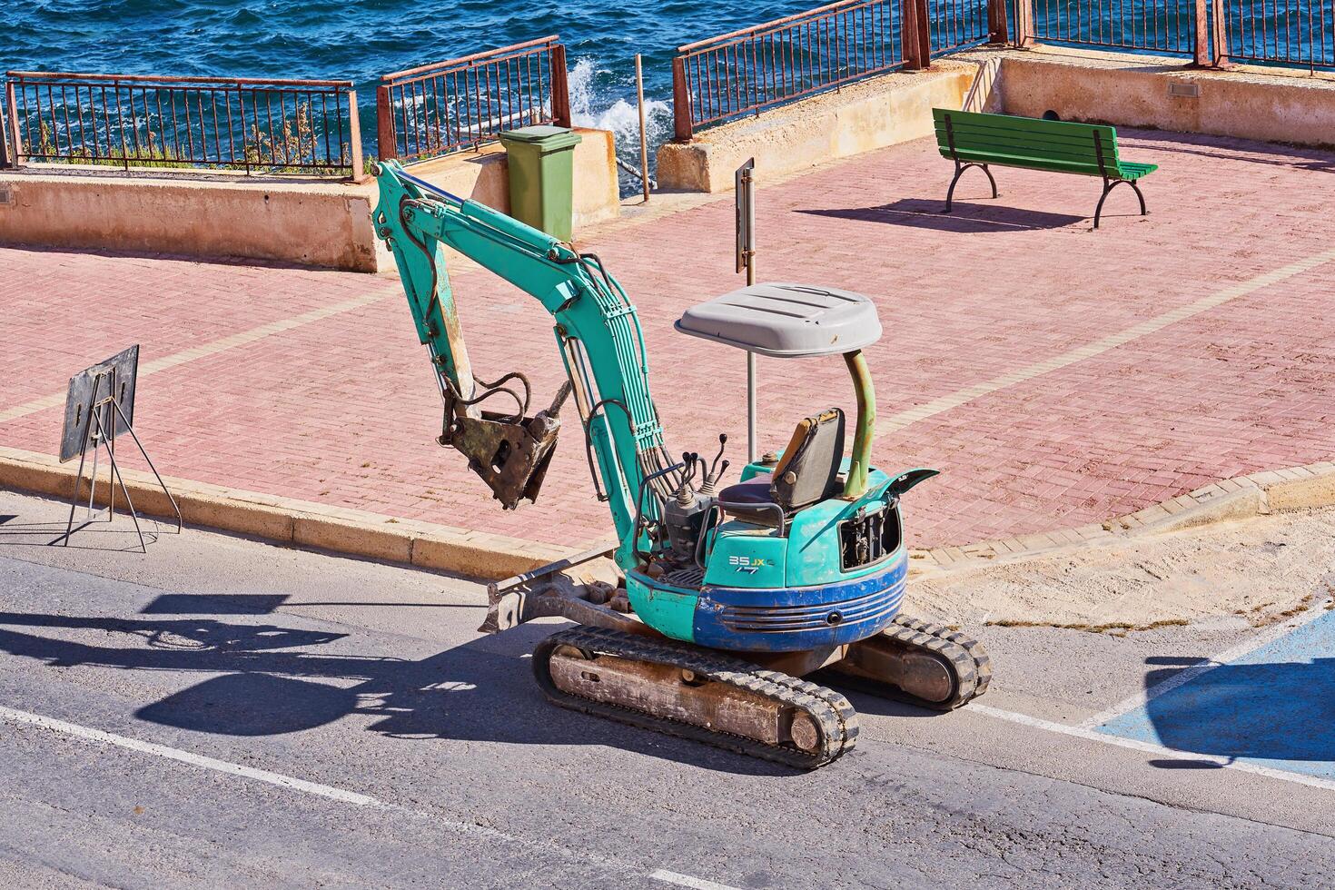 Compact excavator digging holes for palm tree planting as part of an urban landscaping project near a waterfront. Xghajra, Malta-16.06.2020 photo