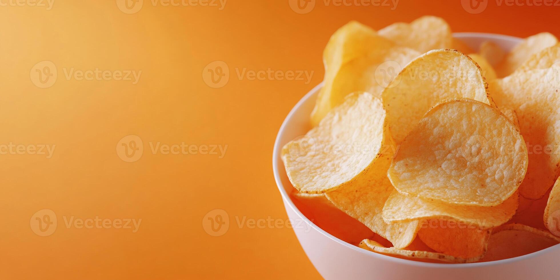 A bowl of crispy potato chips against an orange background. photo