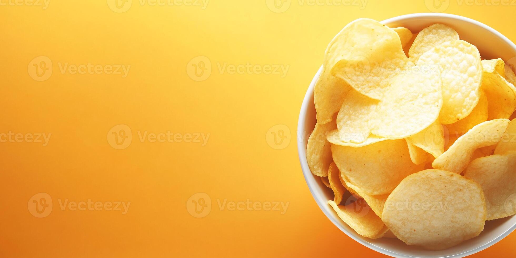 A bowl of yellow potato chips on a bright orange background. photo