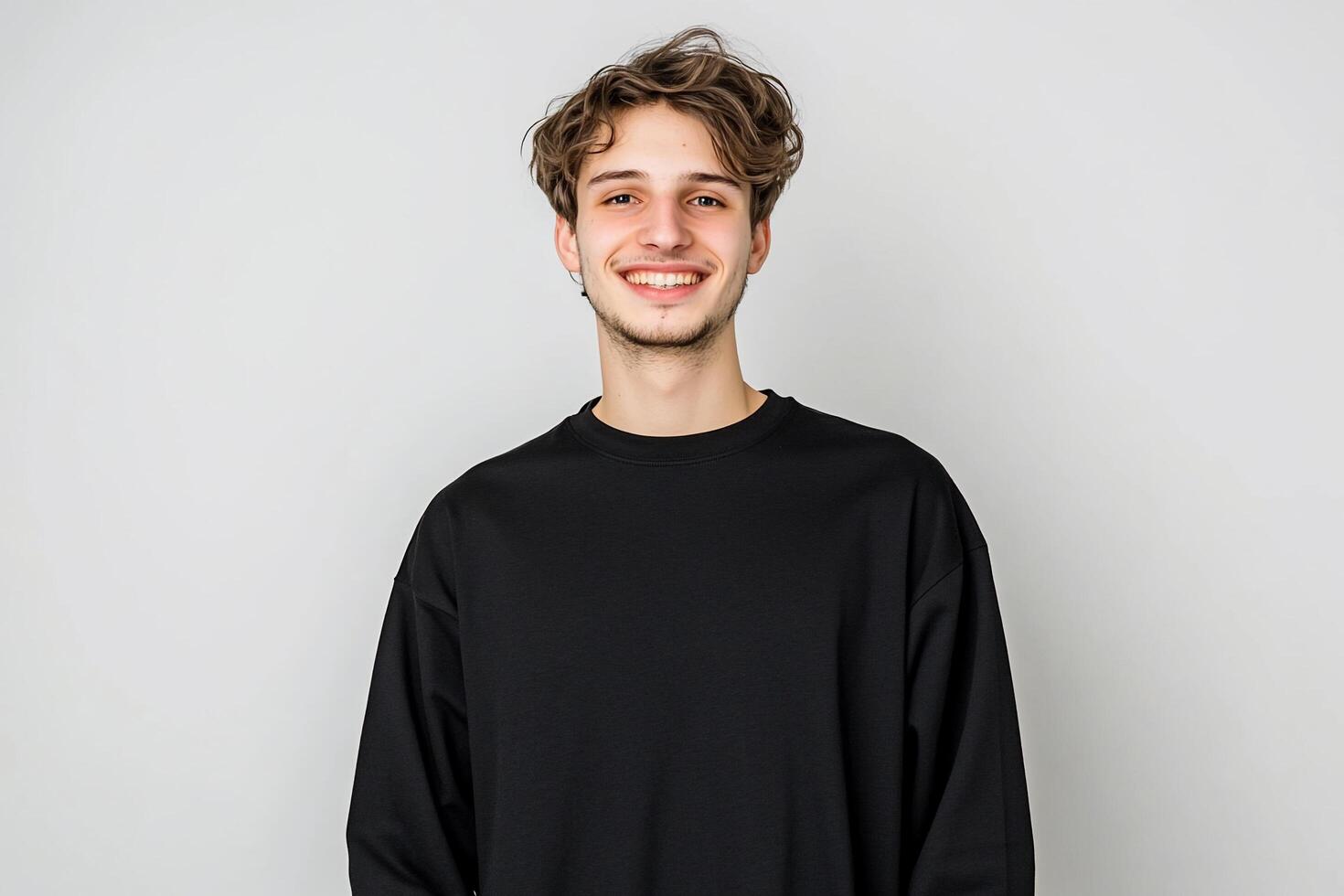 A young man smiles warmly against a plain background. photo