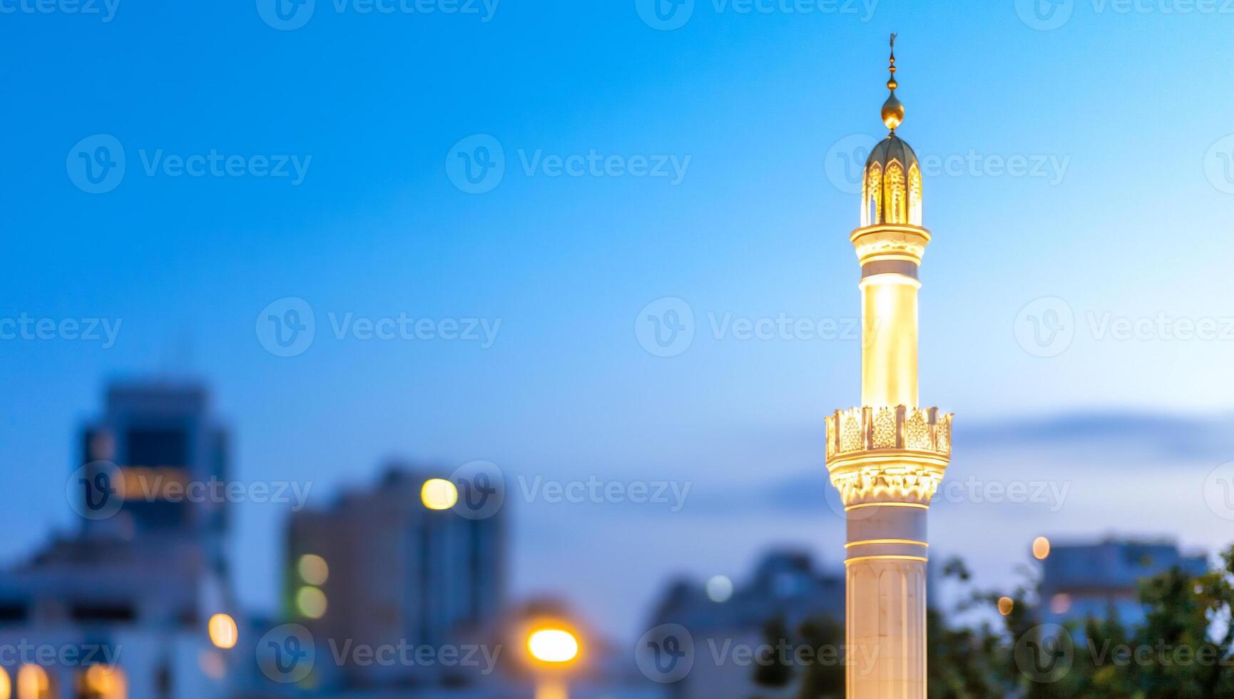 A minaret illuminated against a twilight city skyline. photo