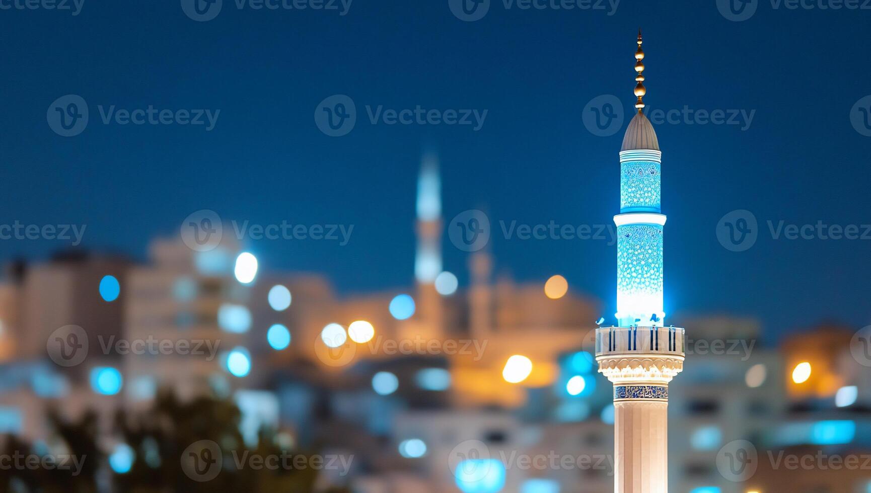 A illuminated mosque minaret at night with a blurred city backdrop. photo