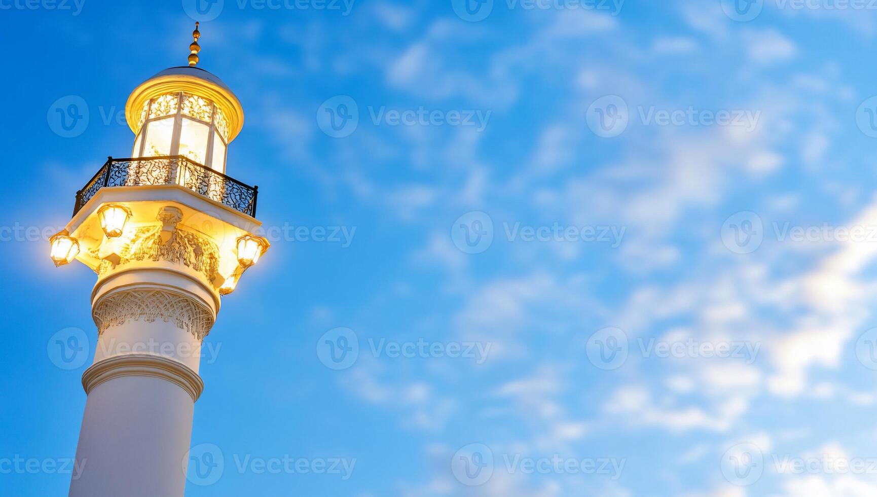 A tall, illuminated minaret against a blue sky, showcasing architectural beauty. photo