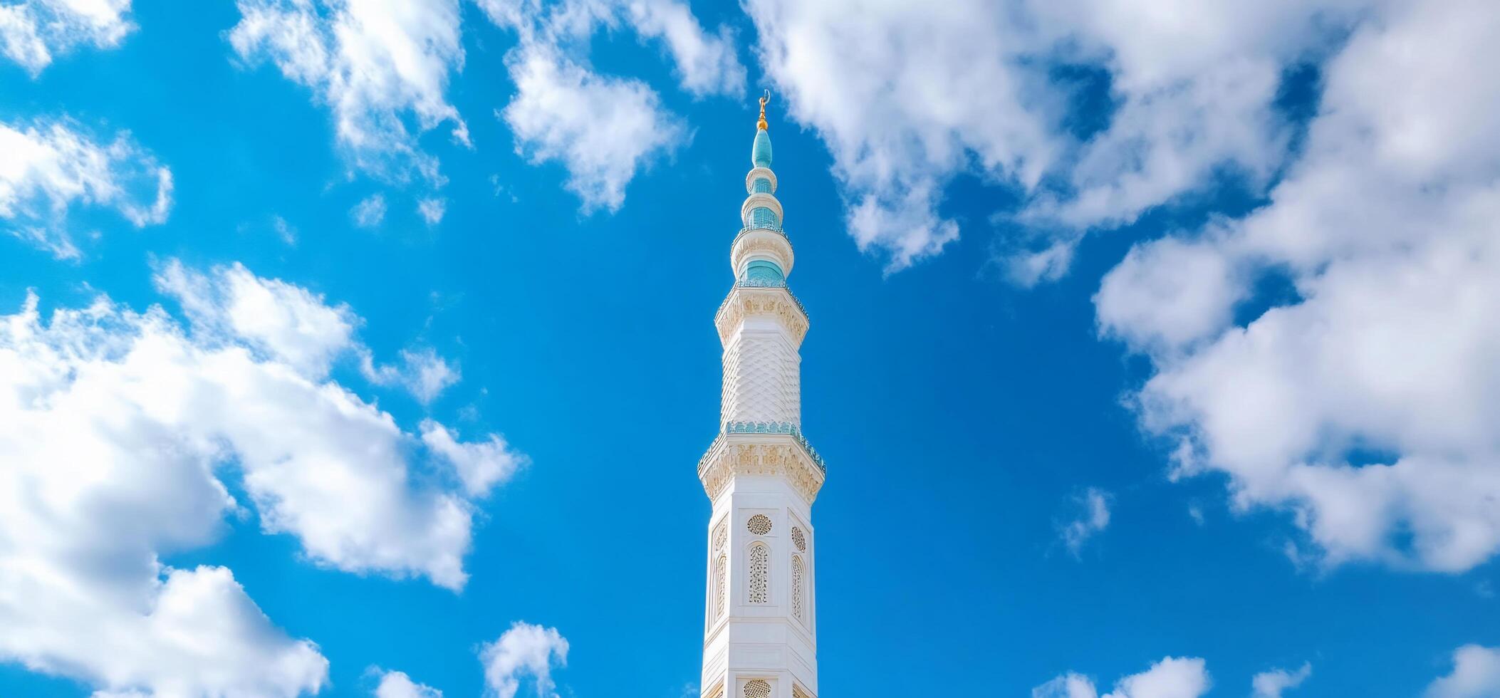 A tall, white mosque minaret against a bright blue sky with clouds. photo