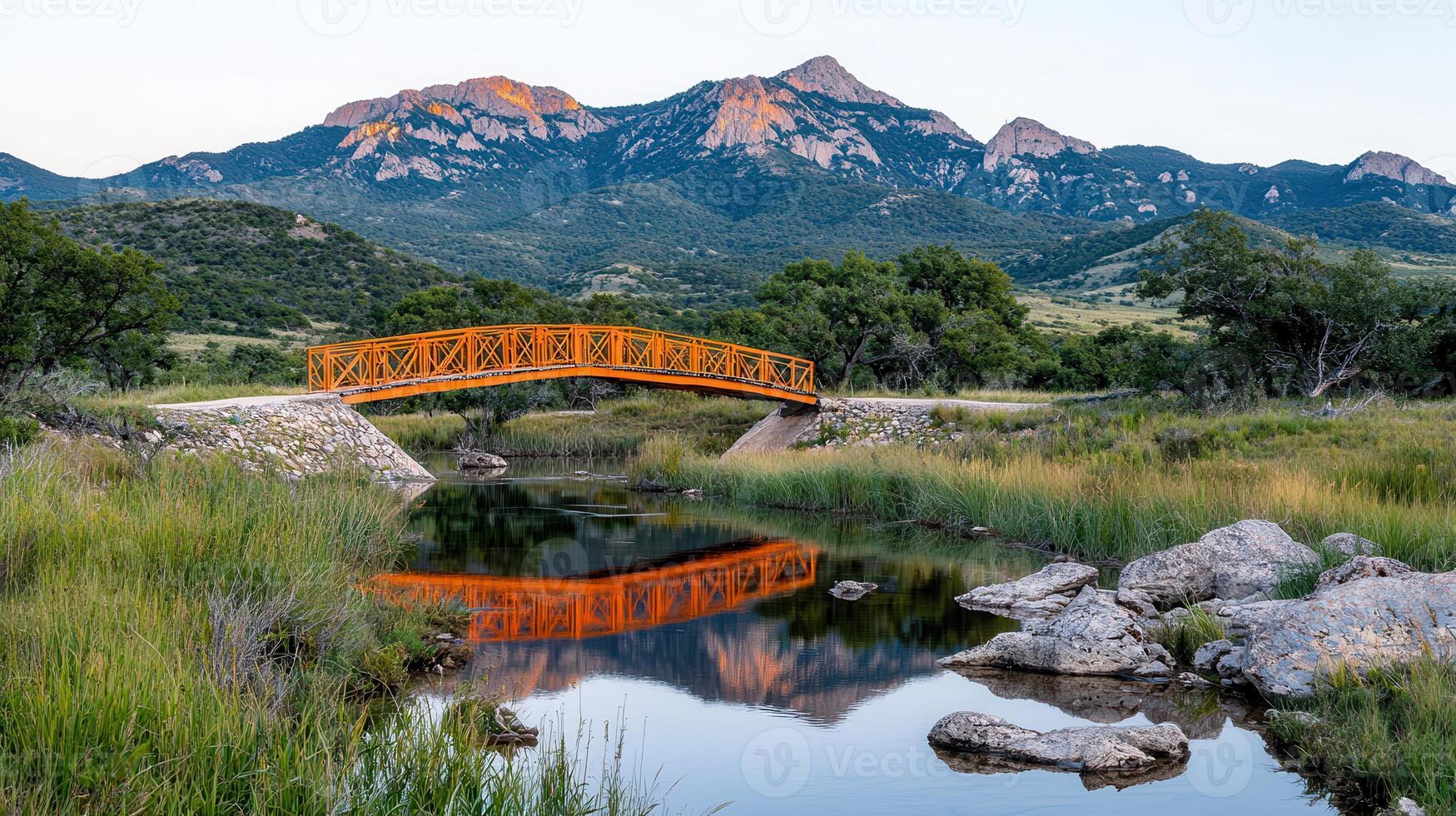Scenic Orange Footbridge Over Calm River with Majestic Mountain Range Background photo