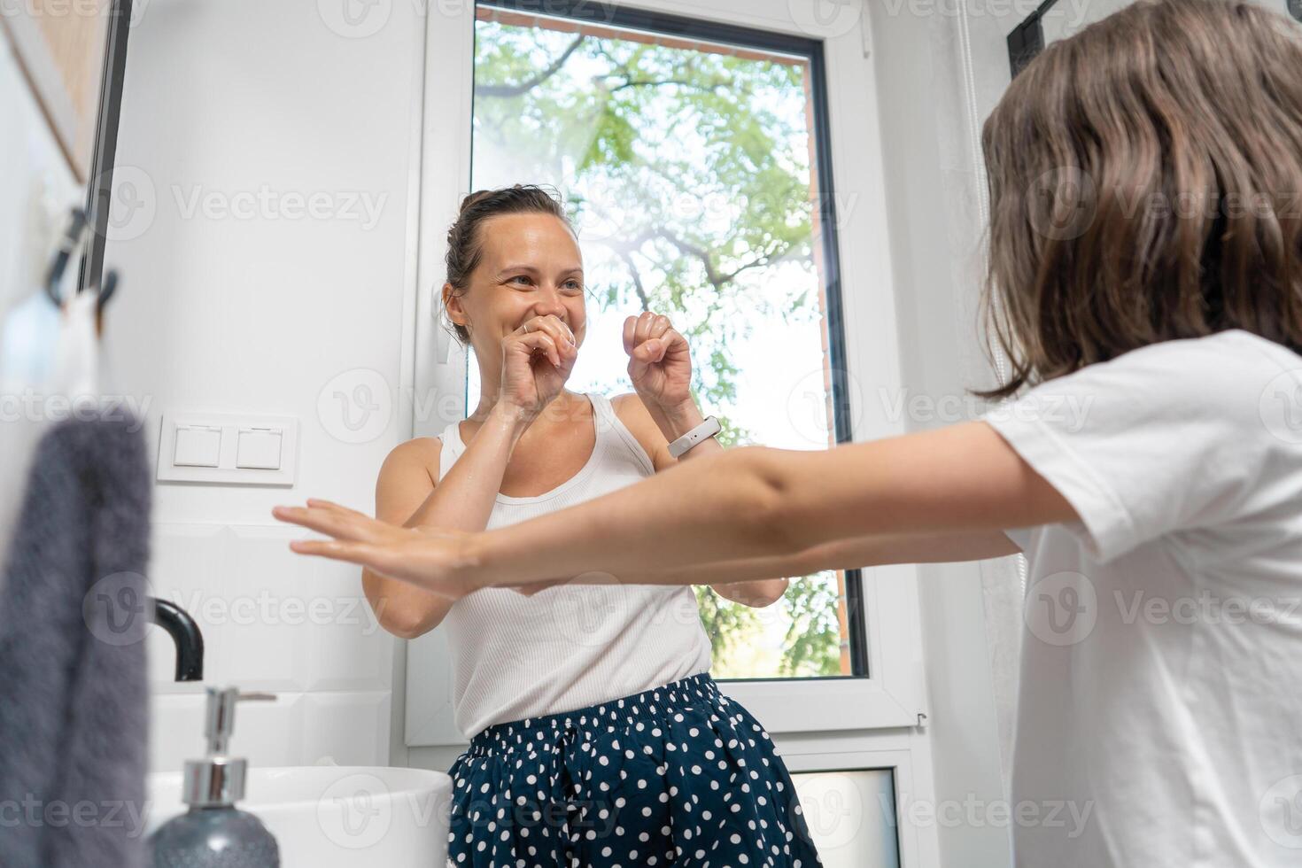 A woman brushing her teeth with a child in the bathroom photo