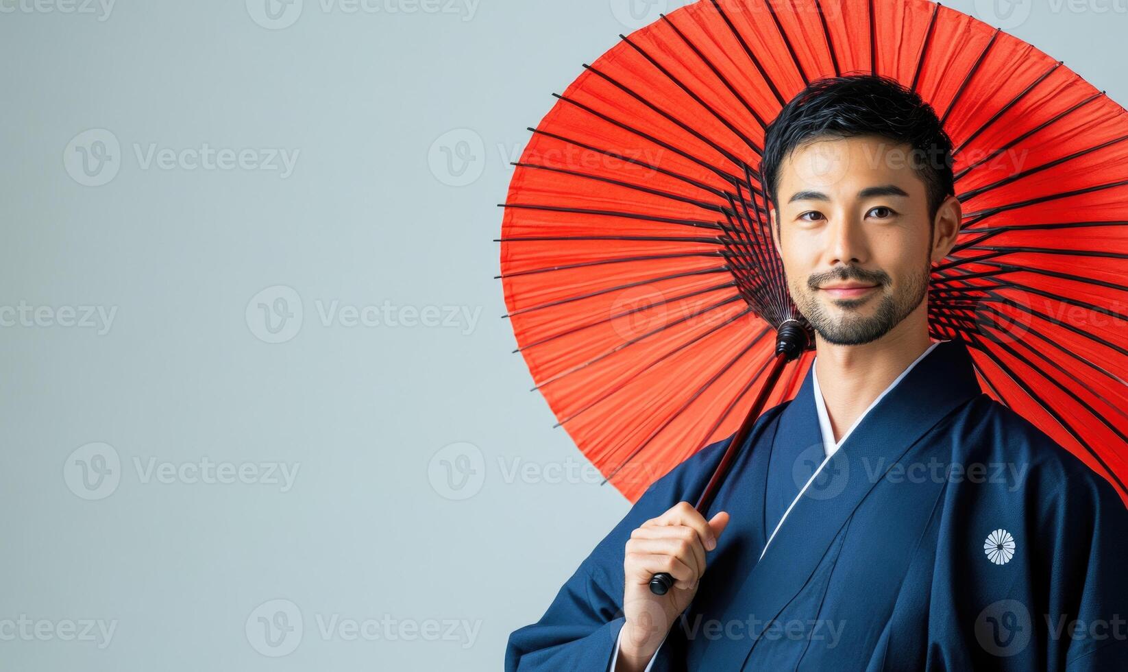 A man wearing a blue kimono is holding a red umbrella photo