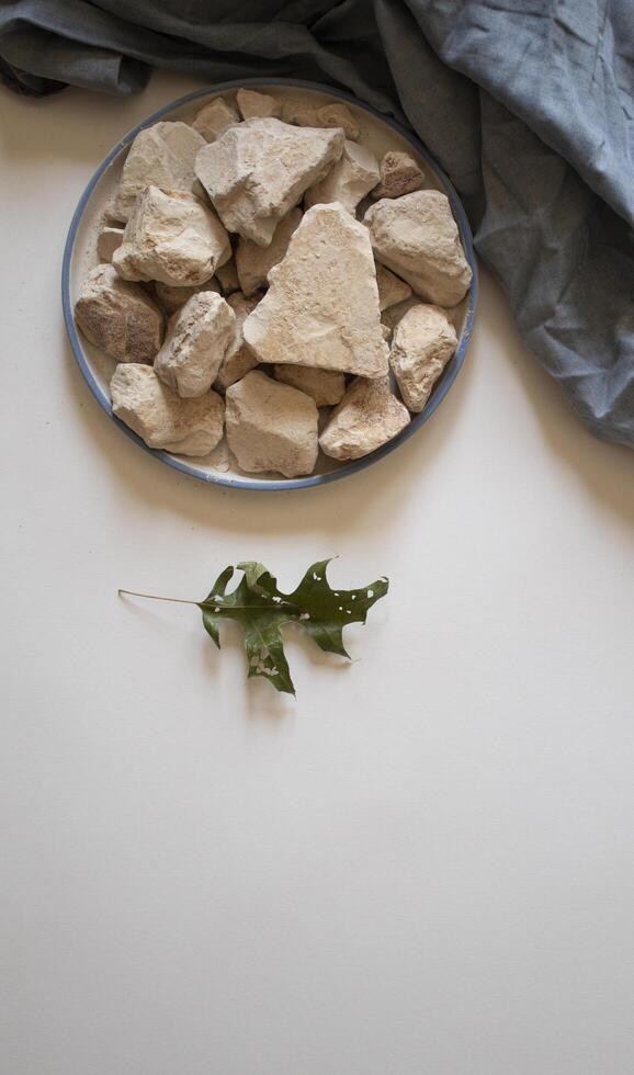 White clay stones with a green leaf on a white background flat lay photo