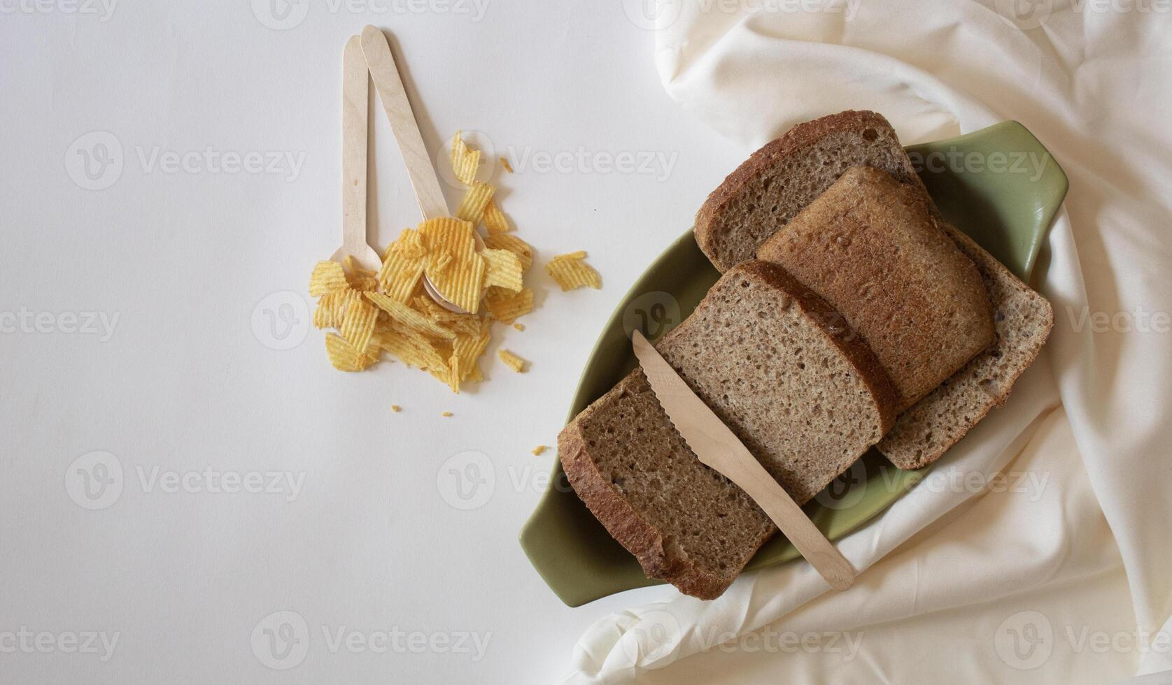 Brown bread slices, spoons and potato chips on a white background photo