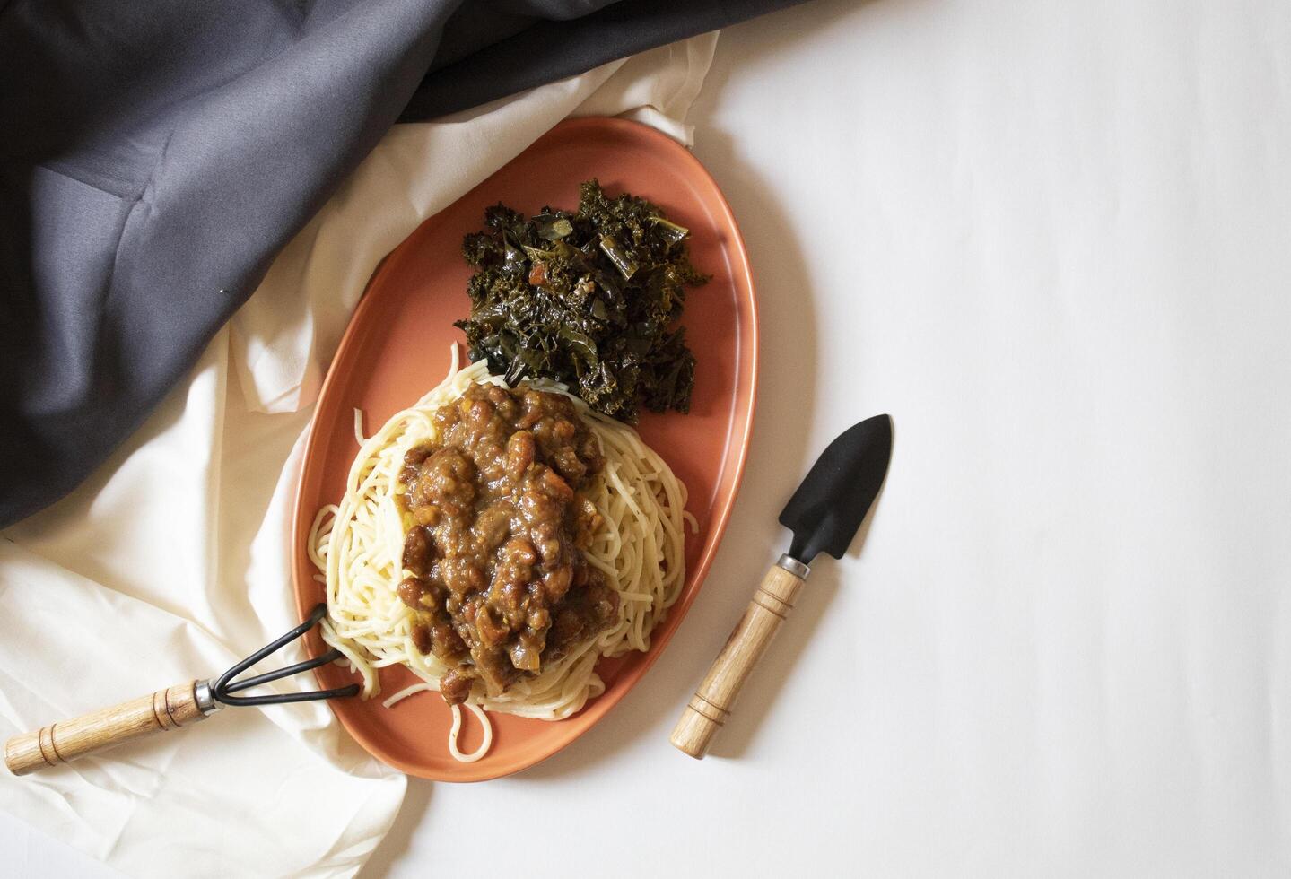 Spaghetti and green vegetables with a small garden fork and shovel on a white background photo