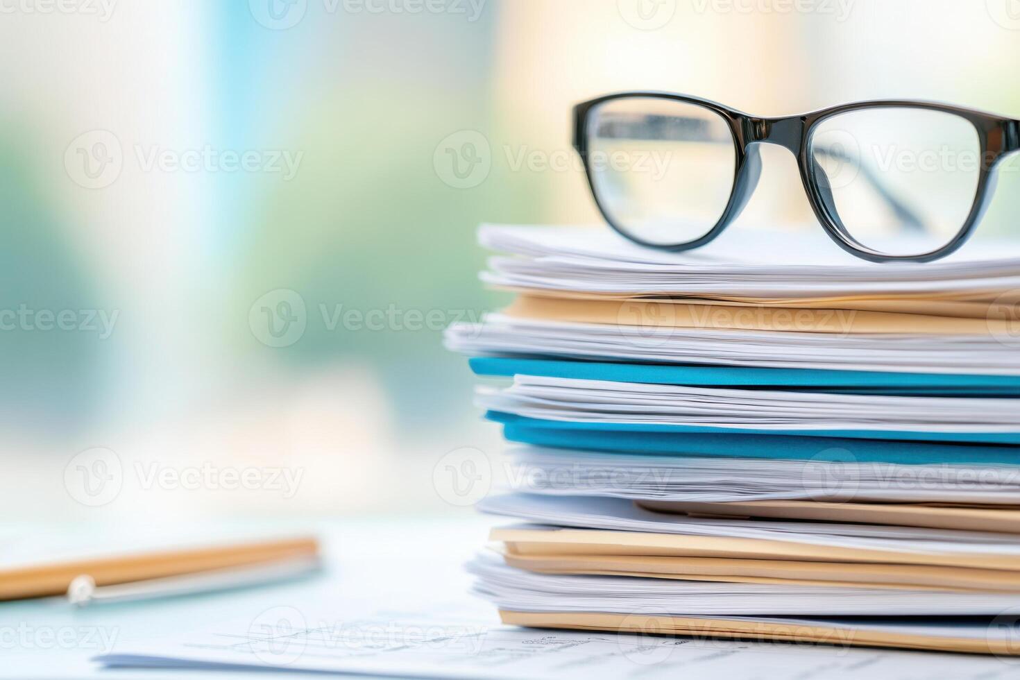Stacked paperwork with eyeglasses resting on the top in a bright office environment during the day photo