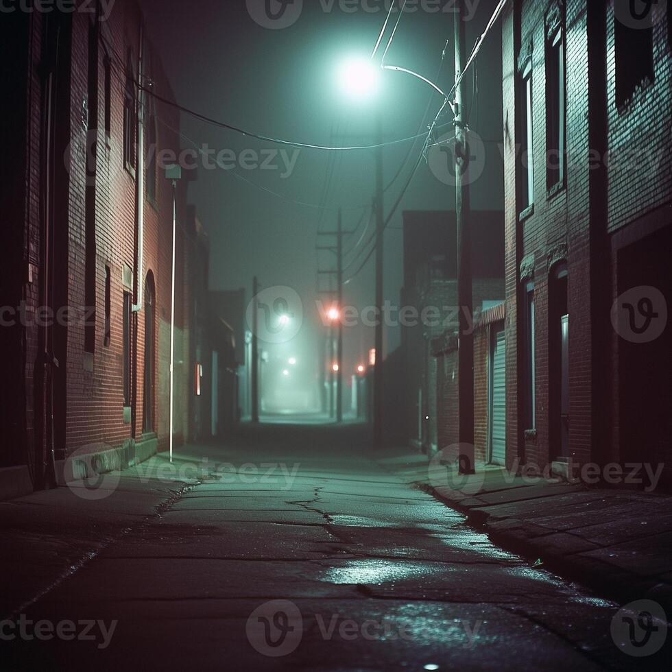 A silent alleyway at night, surrounded by tall brick buildings. Faint streetlights cast dim reflections on the uneven pavement. The mist softens the distant glow, creating a sense of emptiness photo