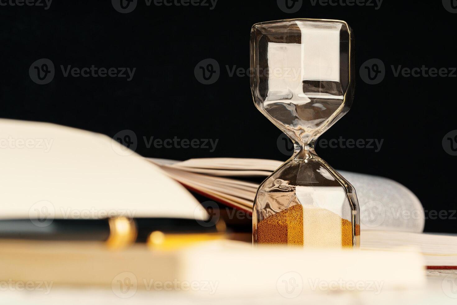 Sandglass on wooden table with opened book close up photo