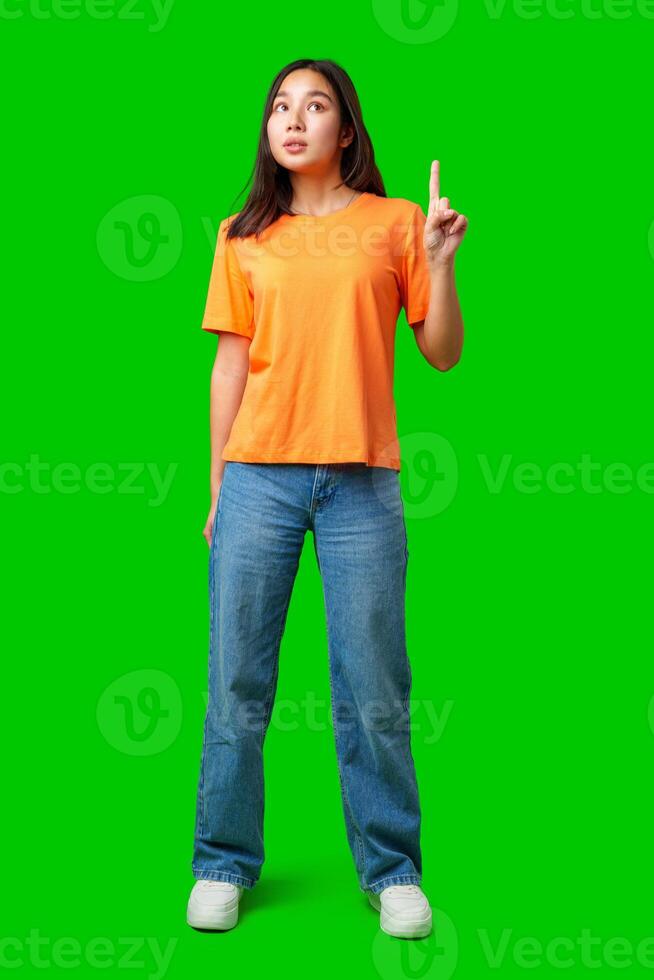 Young woman in bright orange shirt stands with finger raised on green background photo