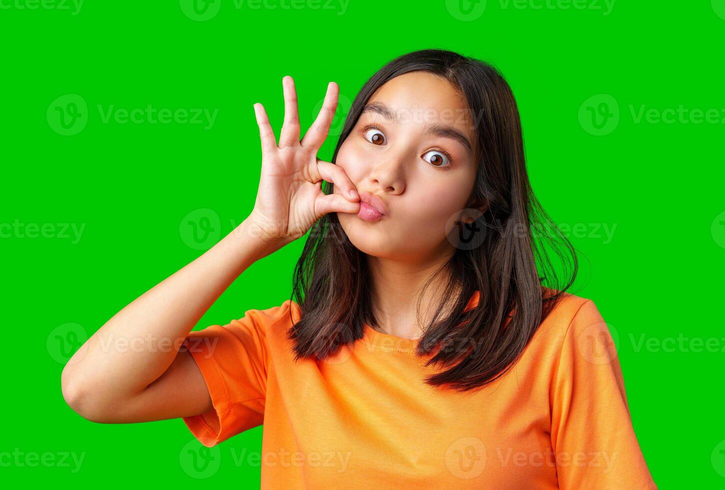 Young girl making a playful gesture against a bright green background at home during the daytime photo