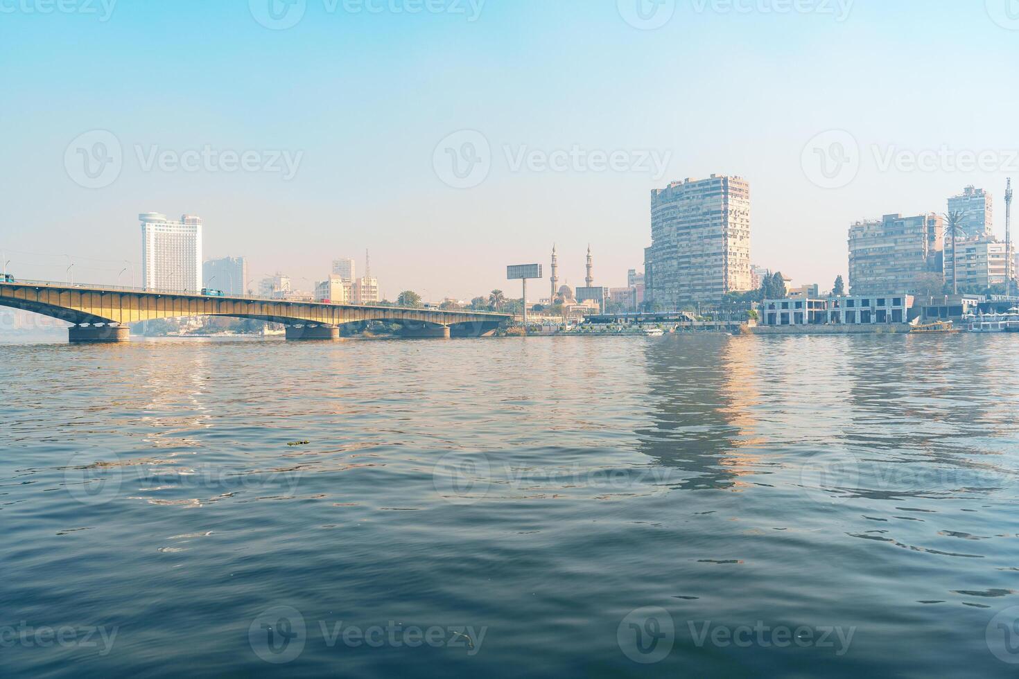 City skyline reflecting on water near a bridge in Cairo during early morning light photo